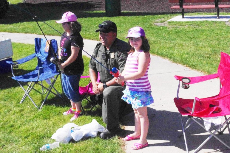 Department of Natural Resources officer Quincy Gowenlock gives advice to Maria and Elizabeth Romero of St. Louis competing in the Pine River Fishing Derby. Image: John Evans, Gratiot County Herald