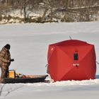 man stands on ice next to hut