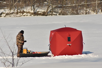 A person standing next to a hut while wearing cold weather fishing gear