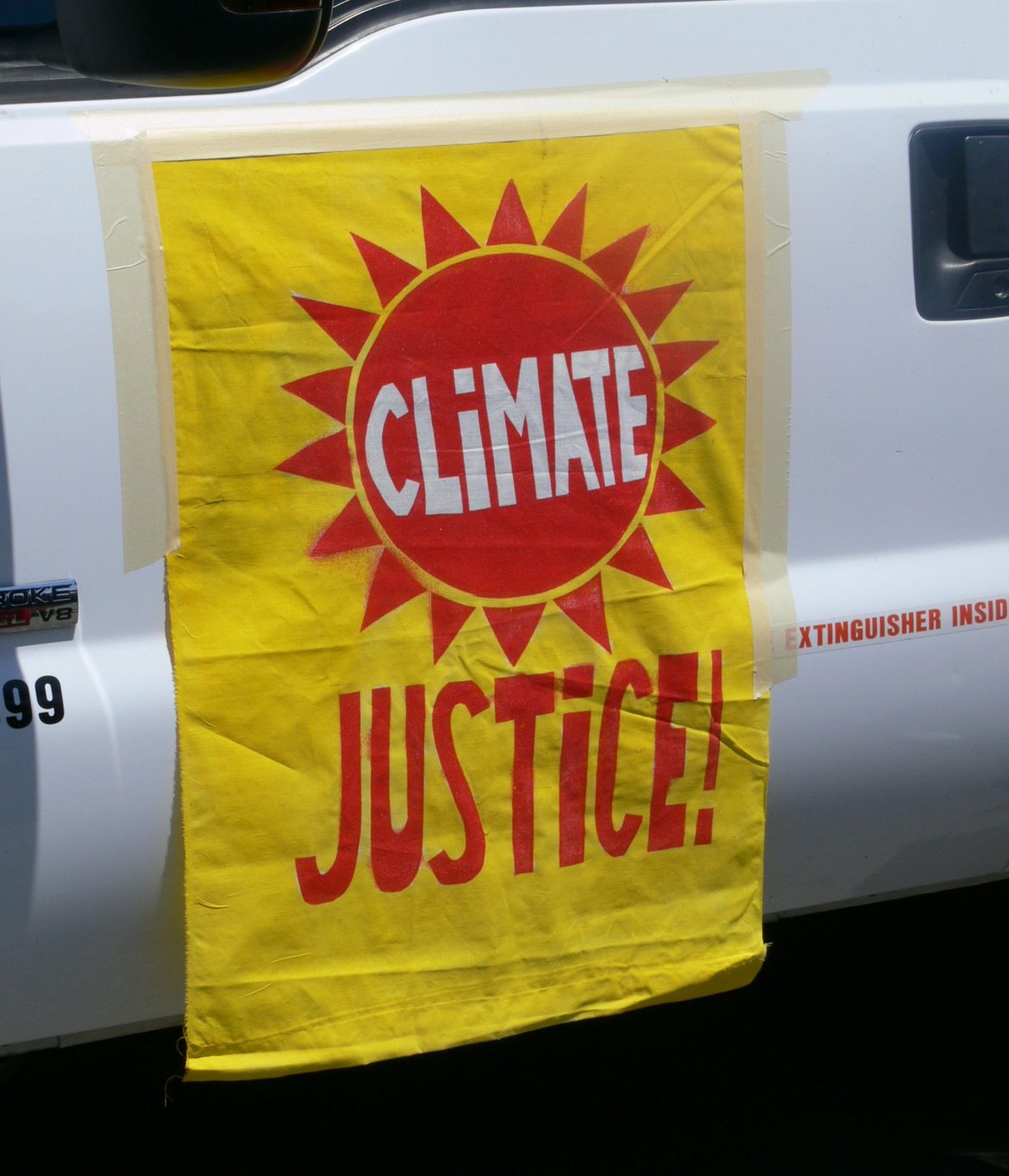 A climate justice banner hanging from the side of a vehicle