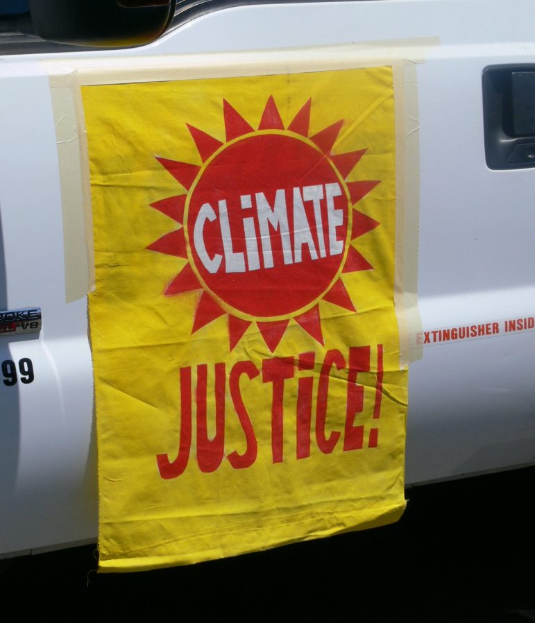 A climate justice banner hanging from the side of a vehicle 