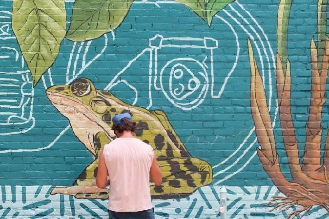 A person stands in front of a wall mural of a frog