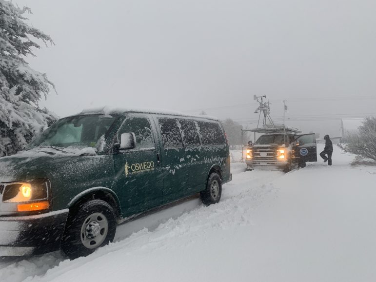 A pair of research vans sit in a road filled with snow as more snow fall from the clouds above