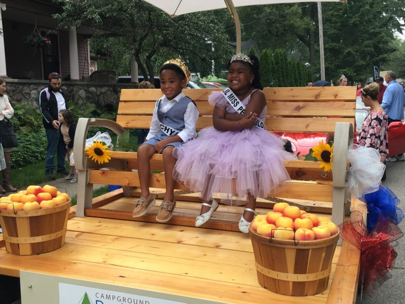 2 children sitting on a bench together with crowns and sashes after winning a competition