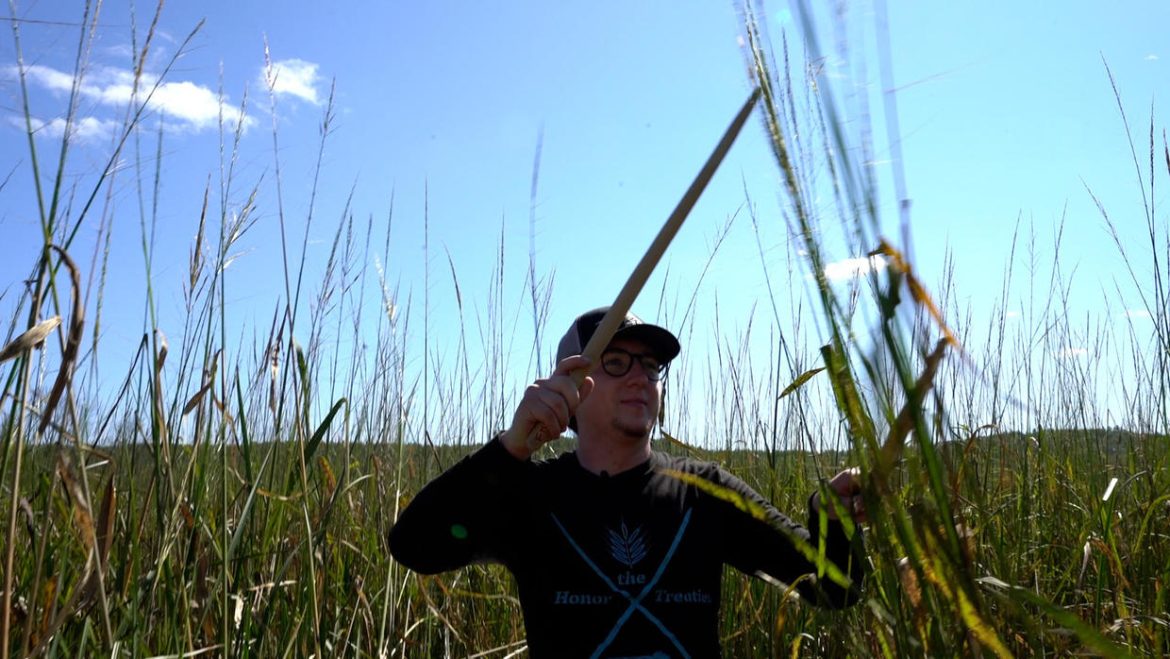 Man holding a "knocking stick," a tool used to harvest manoomin.