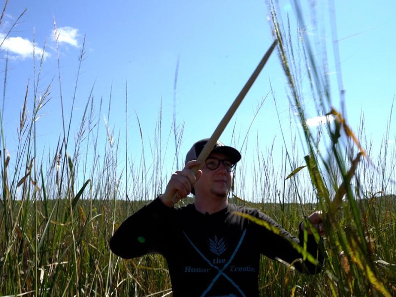 Man holding a "knocking stick," a tool used to harvest manoomin.