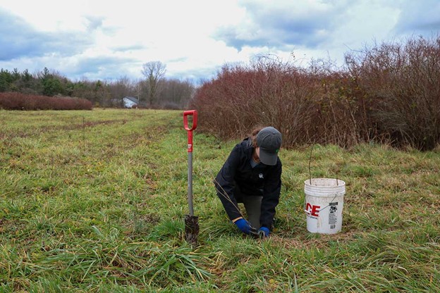 Outdoor Discovery Center staffer digs in the dirt in a field. She is next to a shovel and bucket.