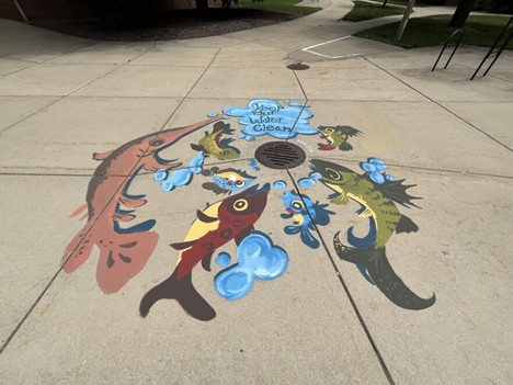 Mural of fish on a sidewalk surrounding a storm drain.