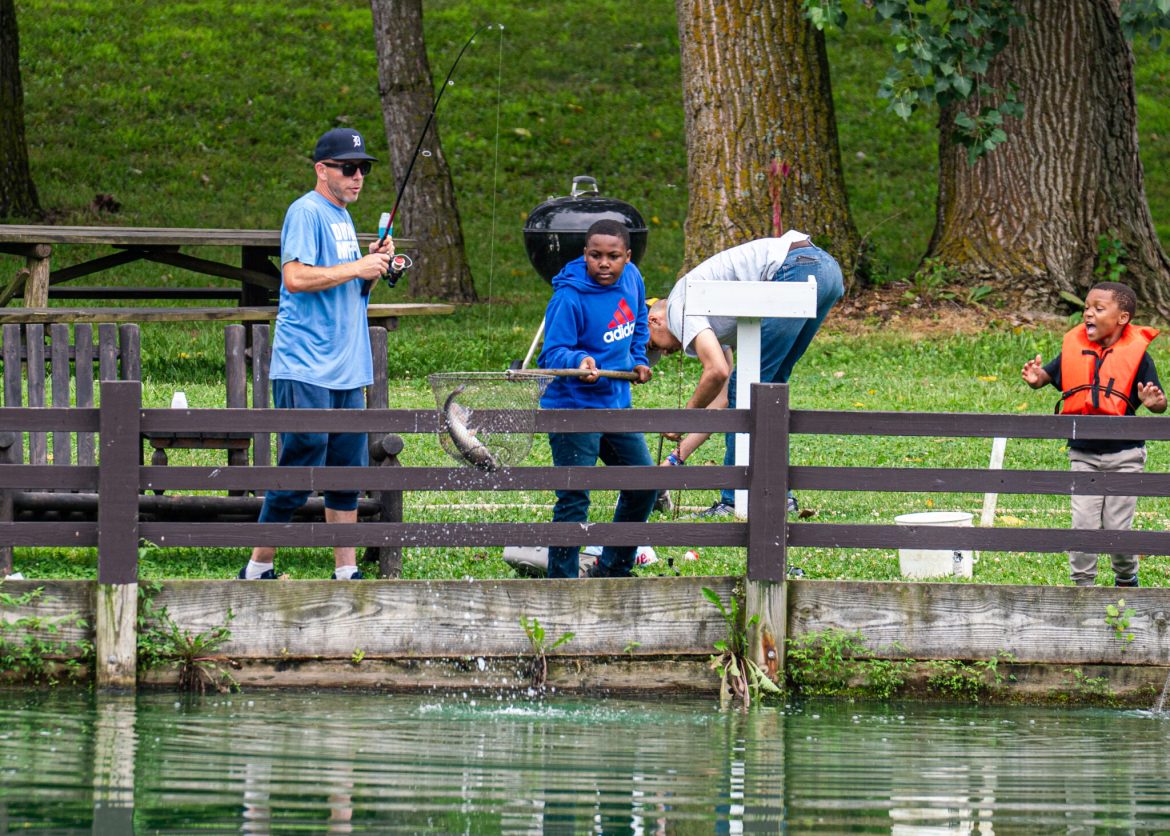 People stand along a fence, fishing at Spring Valley Trout Farm