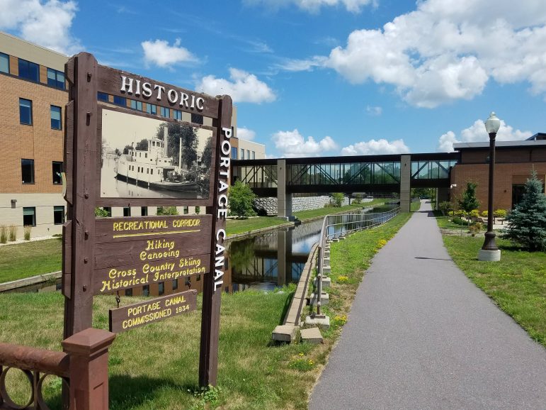 A dark wood historic sign along a paved trail