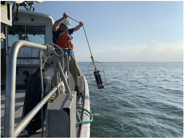 A researcher on a boat lowers a water sampling device into a lake.