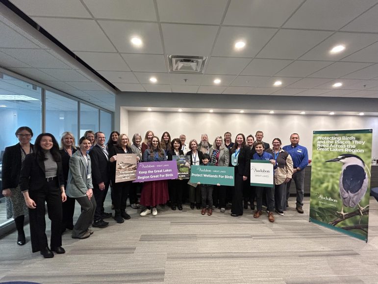 A group of people standing beside an Audubon sign. 