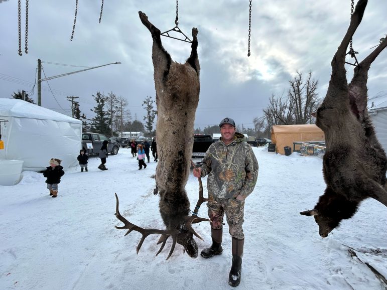 A man in camouflage gear poses with a dead elk.
