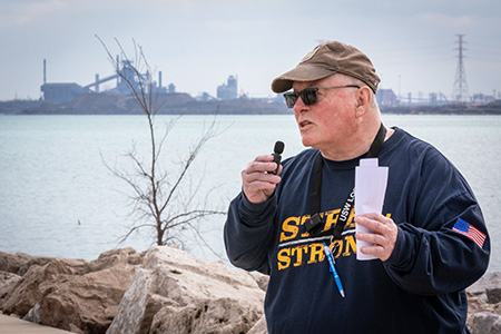 A man speaks in front of a waterfront.